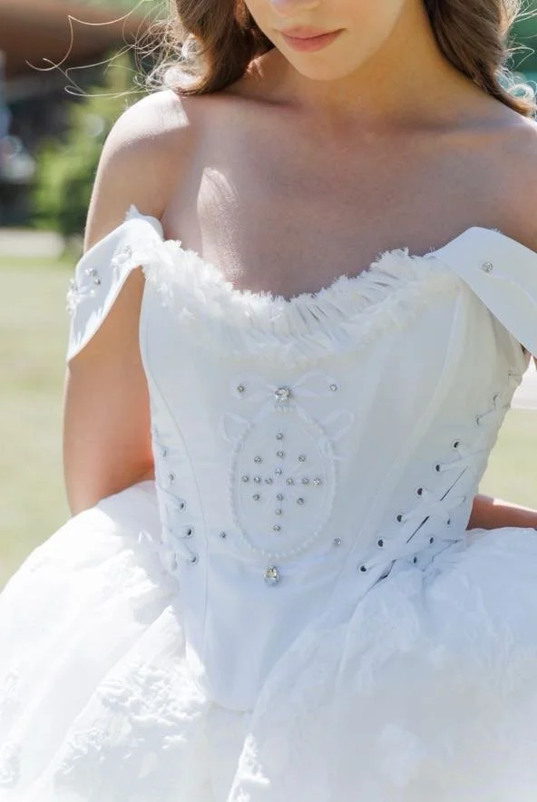 Close-up of a woman wearing a white dress with lace and rhinestone embellishments, outdoors.