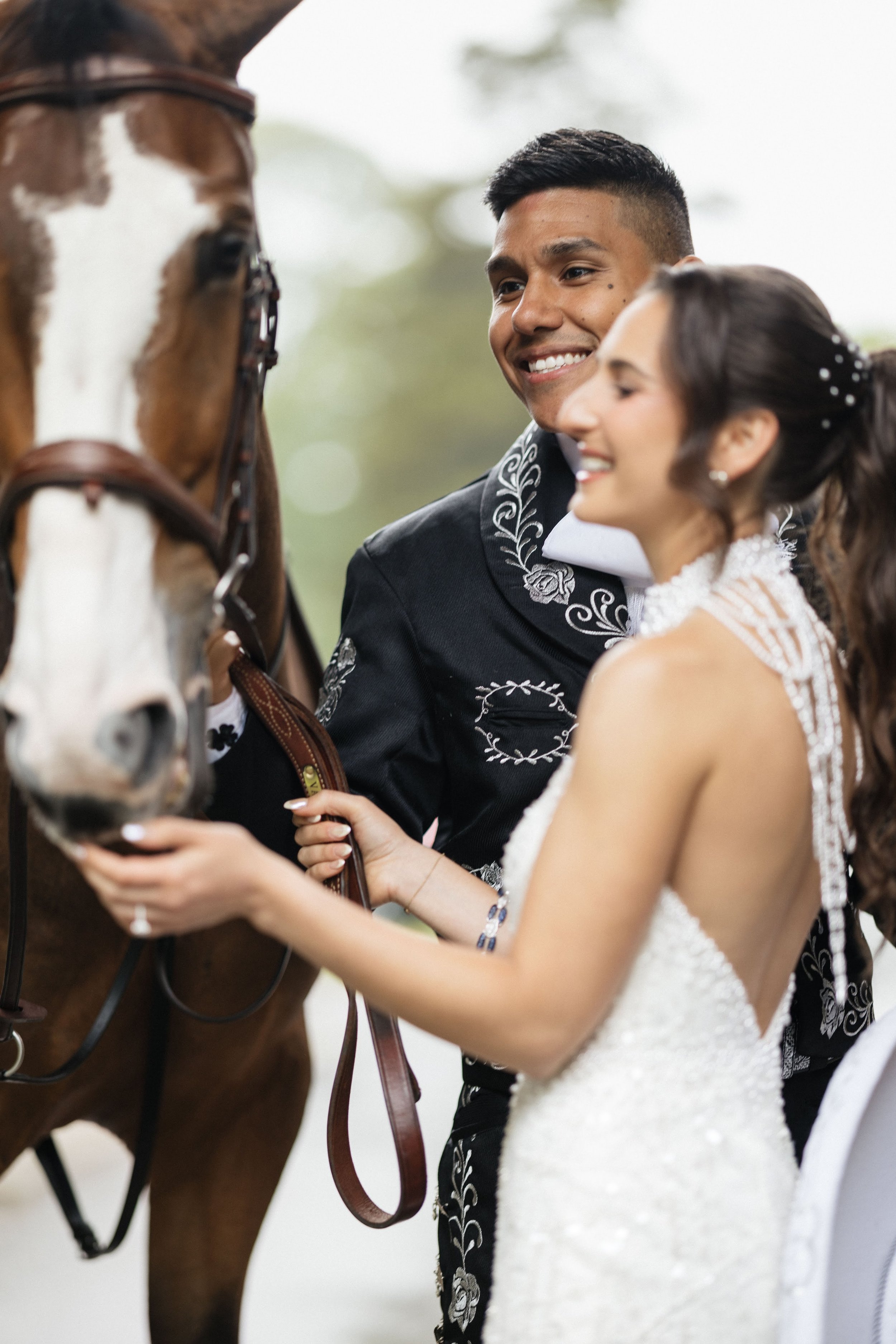 A bride and groom smiling and holding the reins of a horse at their wedding.