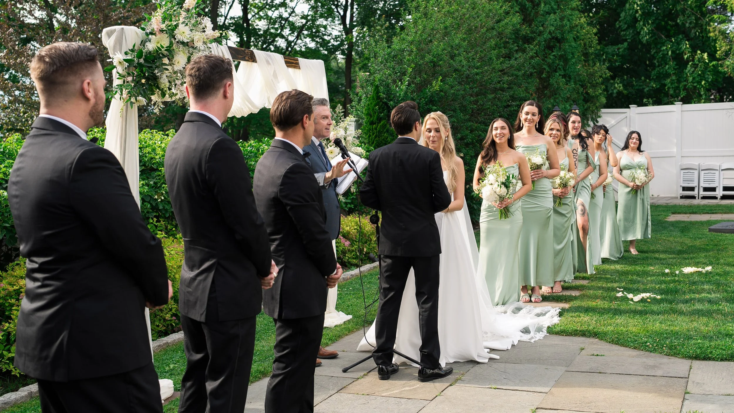 A wedding ceremony taking place outdoors with the bride, groom, officiant, and bridesmaids.