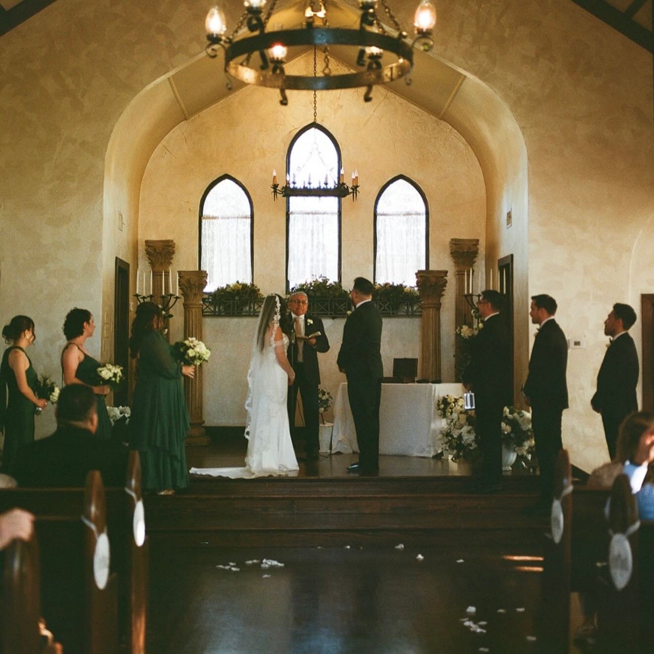 A wedding ceremony taking place inside a church with an altar, bride and groom, officiant, and bridesmaids and groomsmen standing on either side.