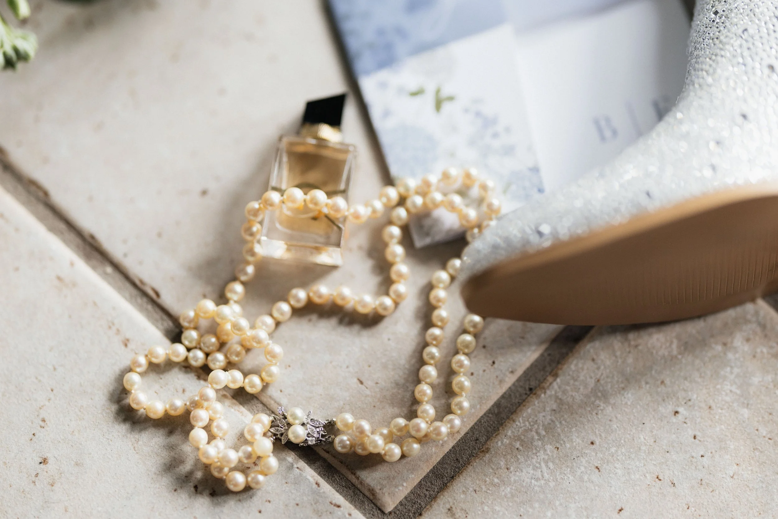 Pearl necklaces and a small perfume bottle on a tiled surface.