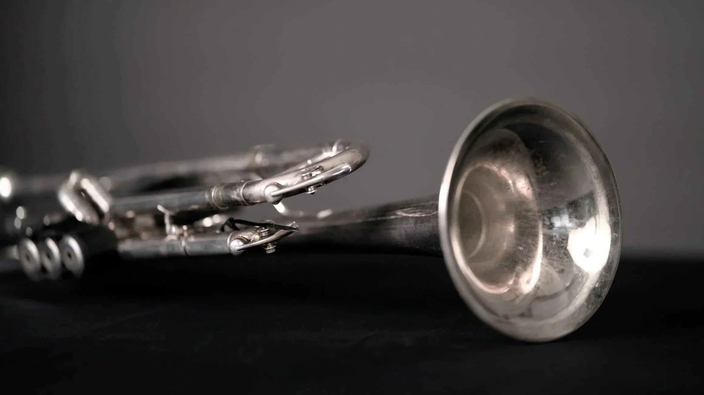 Close-up of a silver trumpet lying on a black surface against a gray background.