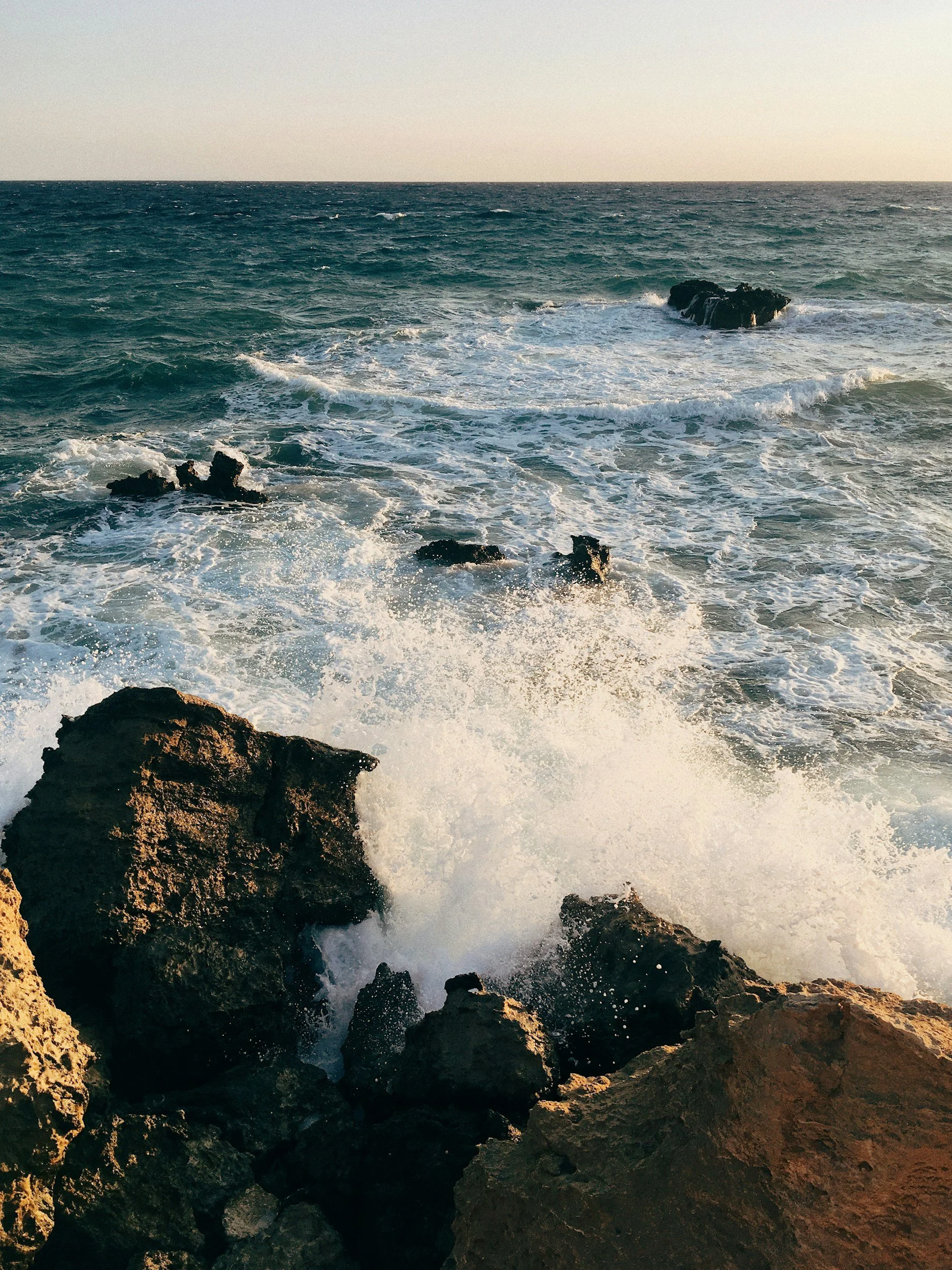Ocean waves crashing against rocky shoreline during sunset.