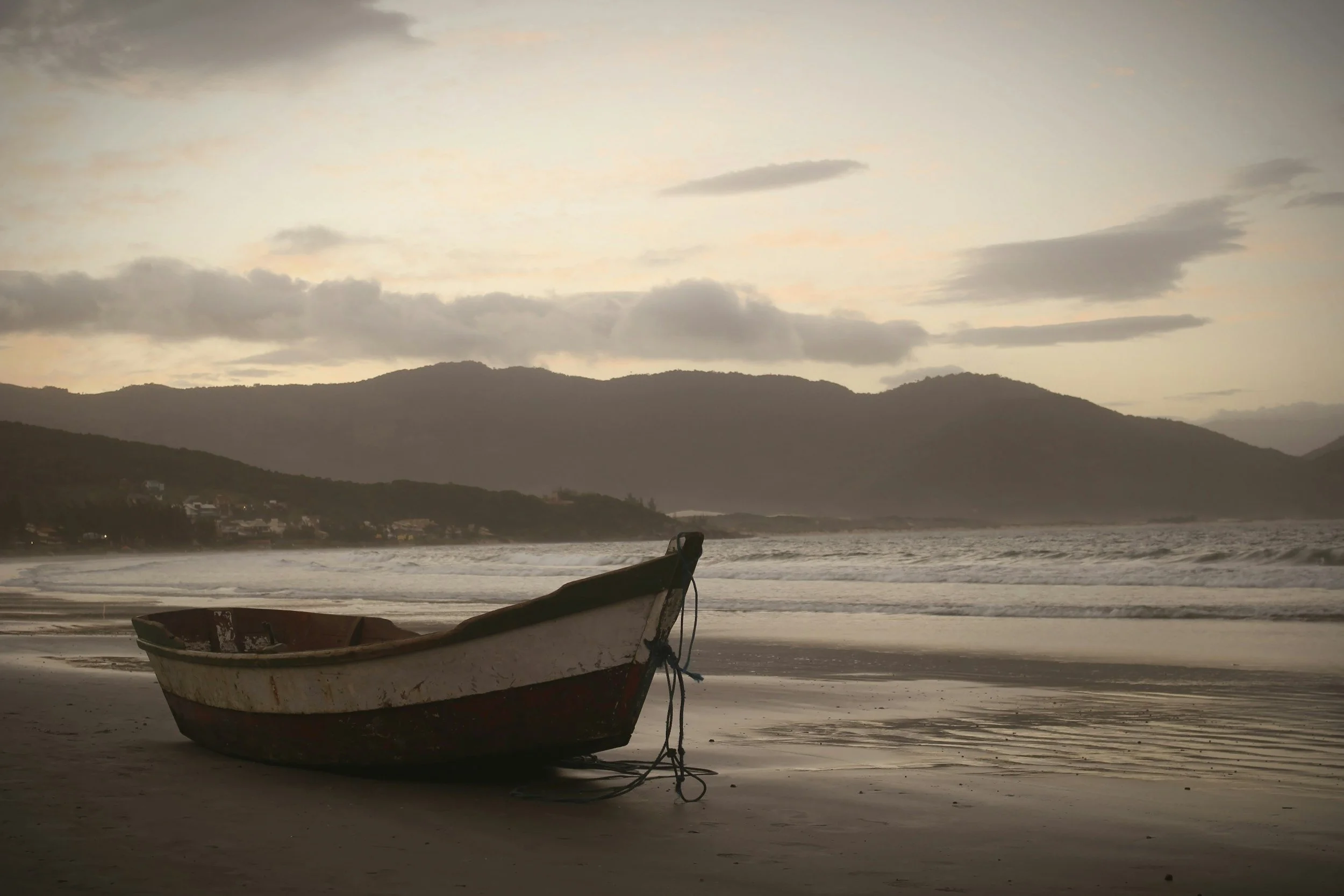A small boat resting on the beach with mountains and cloudy sky in the background during dusk or dawn.