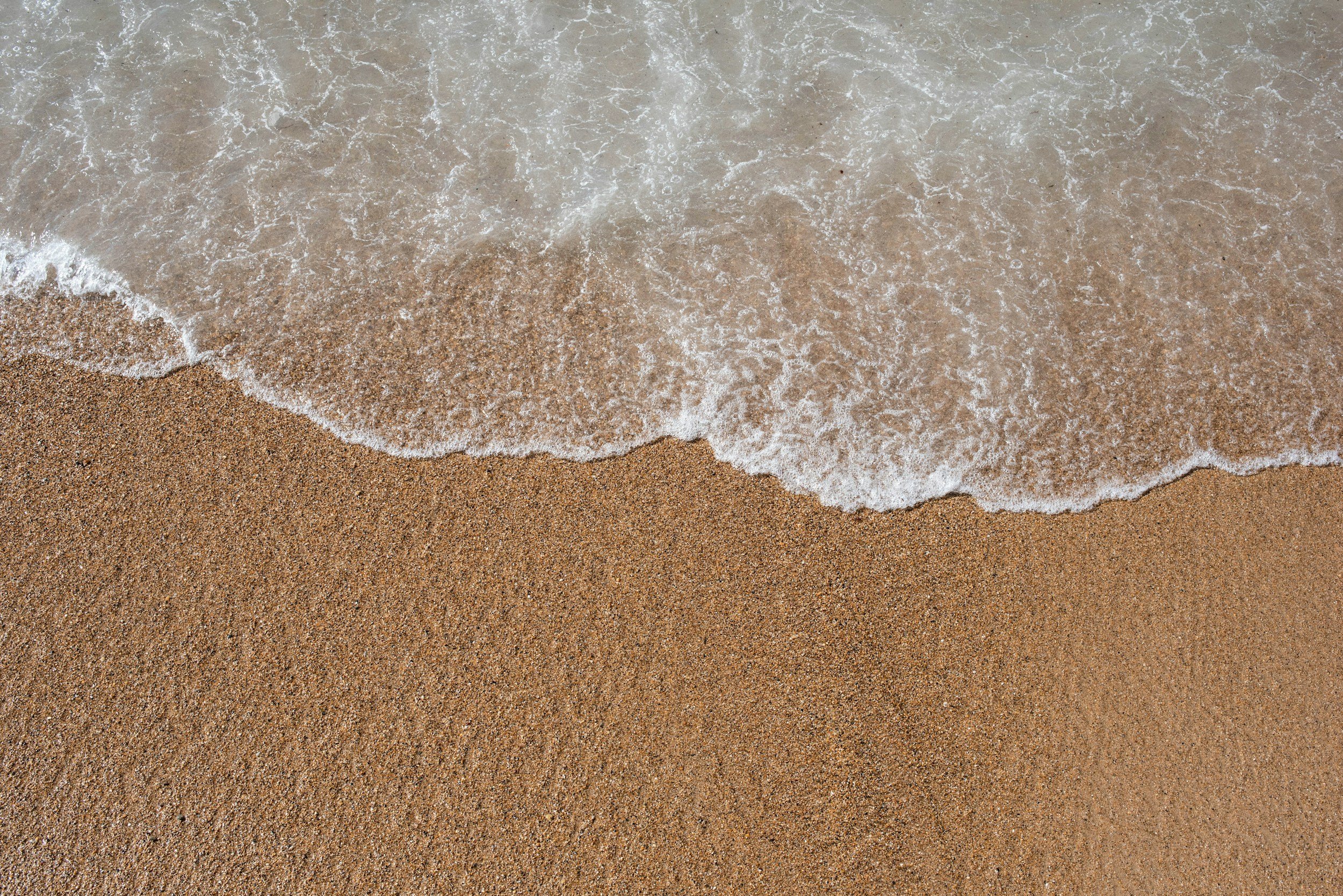 Close-up of wet sand with gentle ocean waves washing onto the shore.