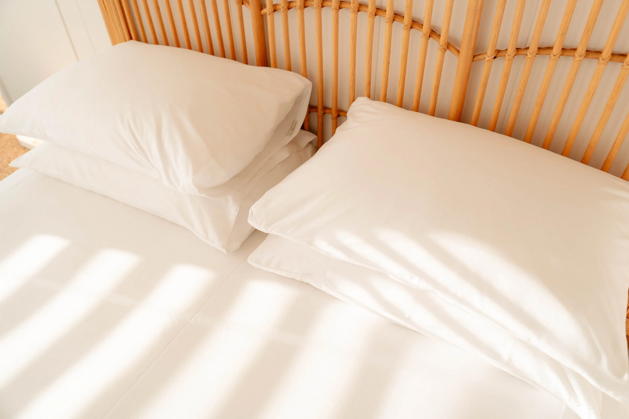 Close-up view of a neatly made bed with white sheets, two pillows, and a wooden headboard with a natural finish.