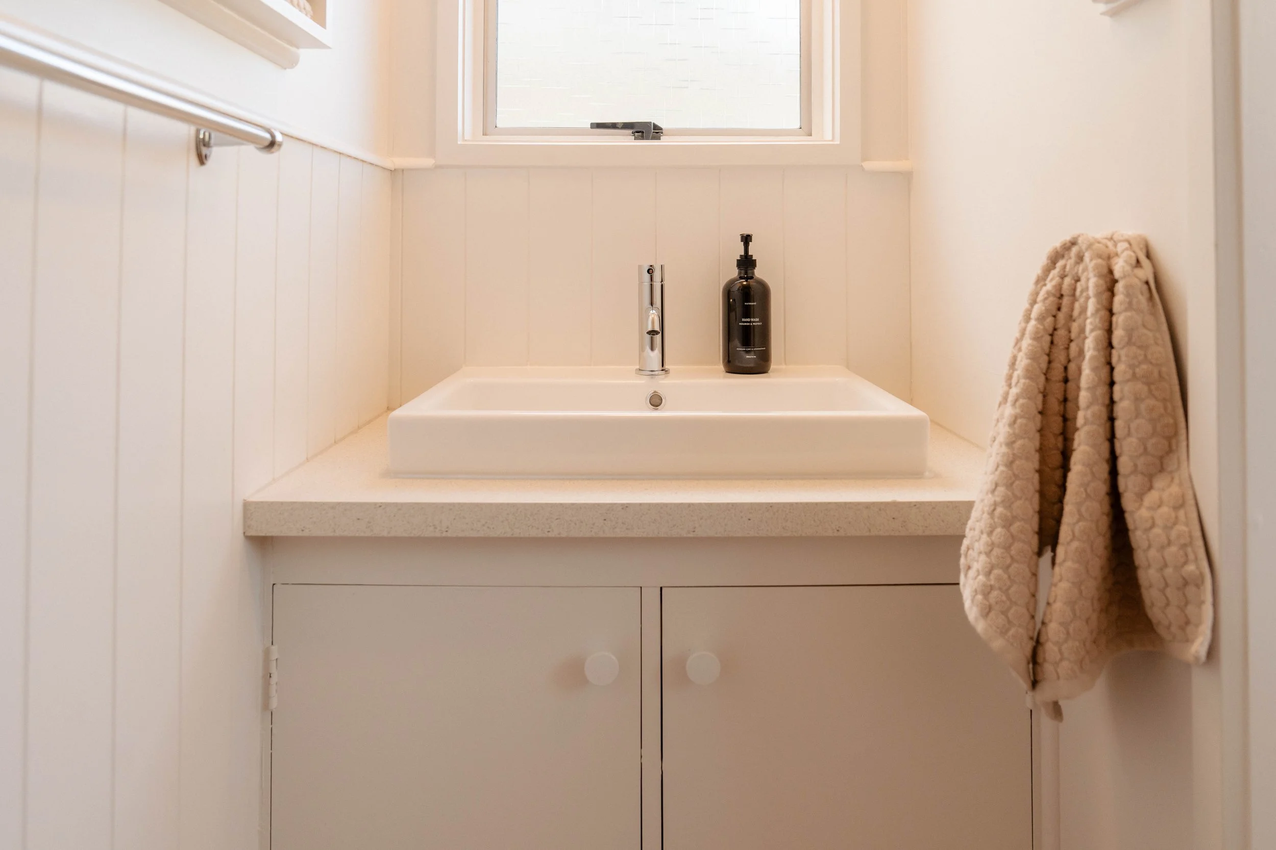 A bathroom sink with a chrome faucet, a black soap dispenser, and a beige textured towel hanging on the right side.