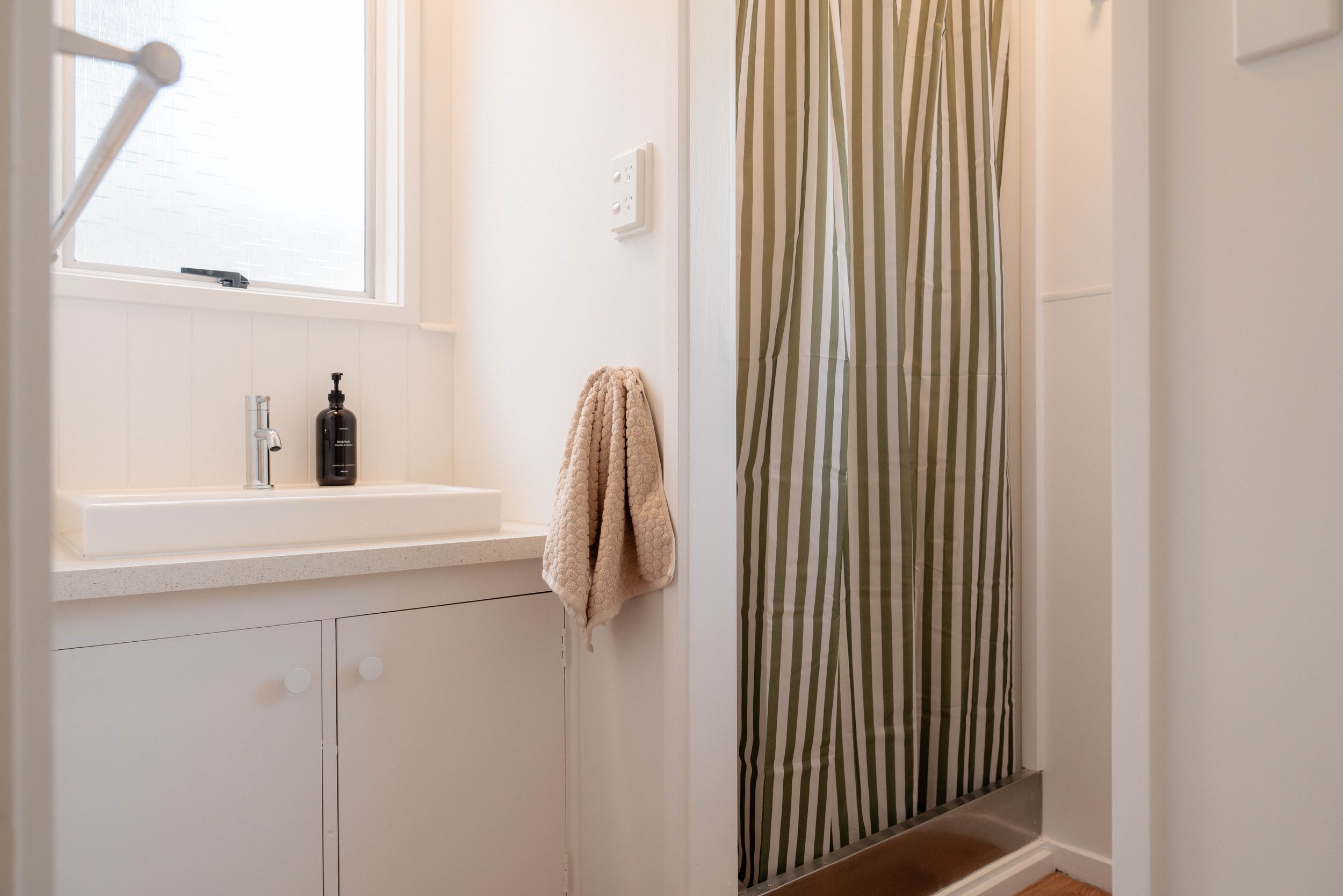 Bathroom with a window, a sink with a black soap dispenser, a beige towel hanging, and a striped shower curtain.