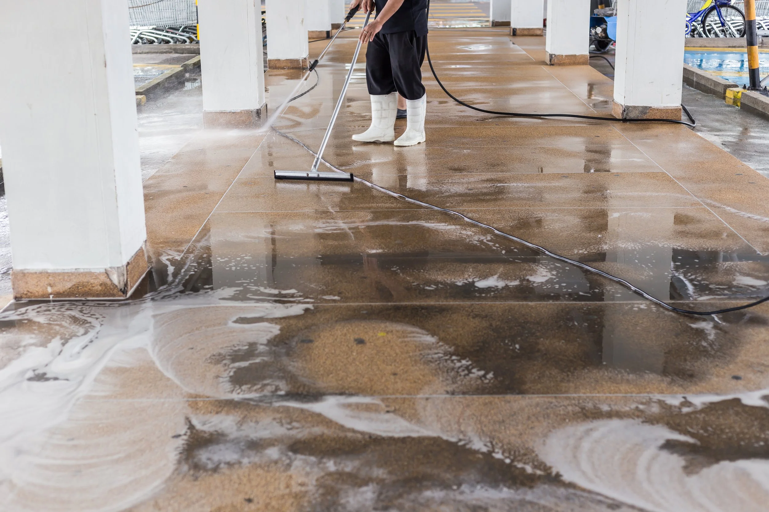 Person cleaning wet floor with a squeegee in an outdoor parking garage area.