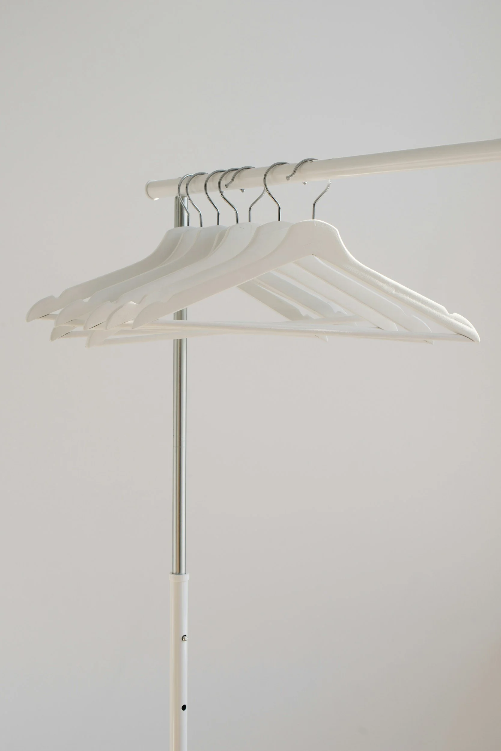 A set of empty white hangers hanging on a white clothing rack against a plain light background.
