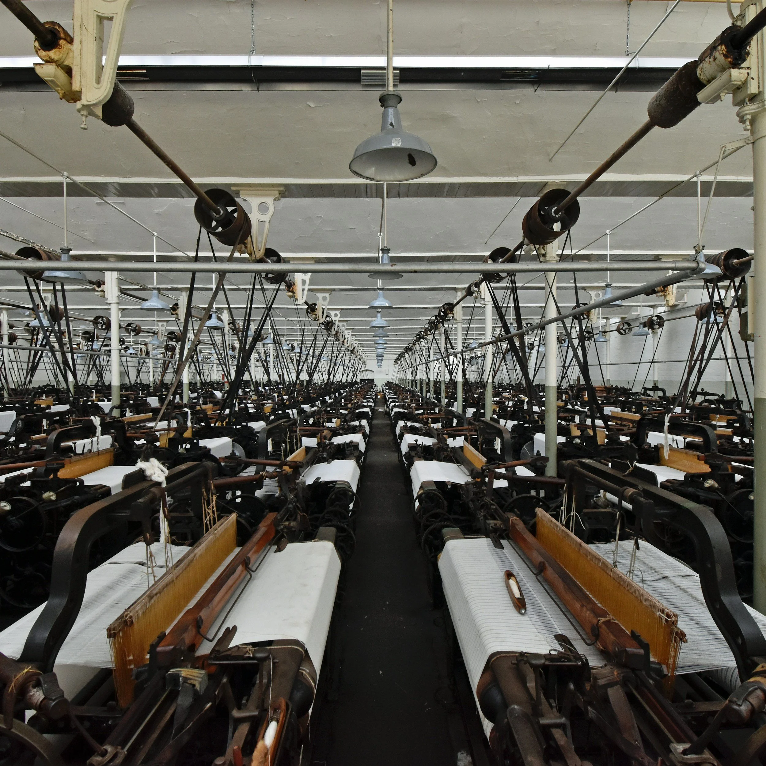 An empty factory with rows of sewing machines and industrial lights hanging from the ceiling.