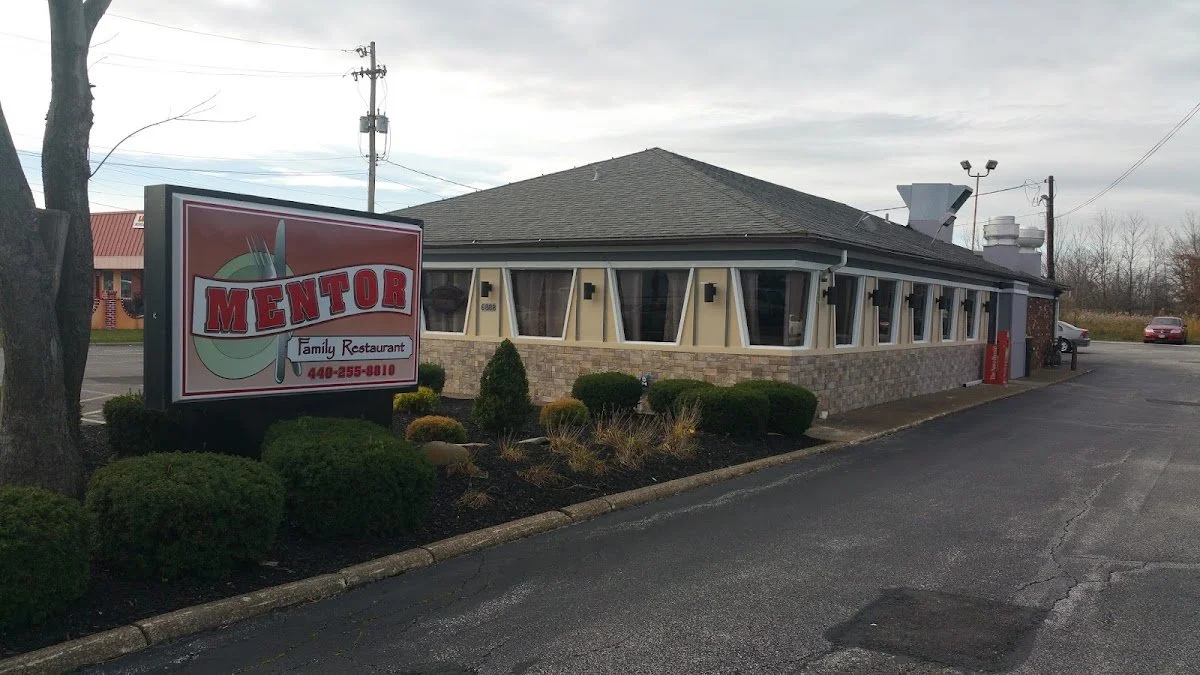 Exterior of a restaurant named Mentor Family Restaurant with a sign in the parking lot and landscaped bushes in front.