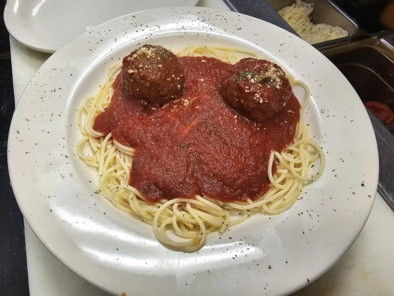Spaghetti with two meatballs covered in tomato sauce, garnished with grated cheese and black pepper on a white plate.