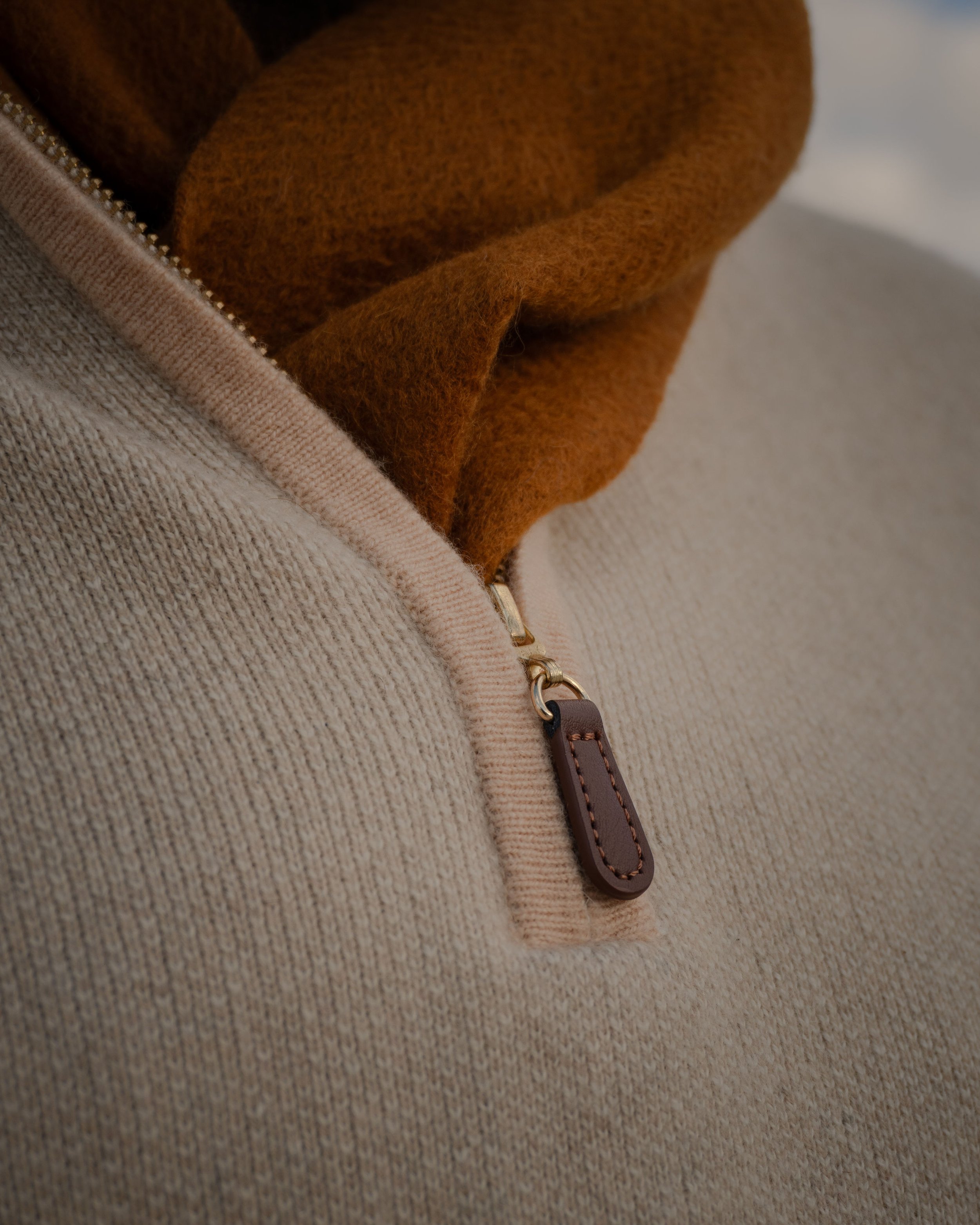 Close-up of a beige and brown jacket with a zipper and a leather pull tab.