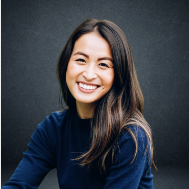A young woman with long brown hair smiling, wearing a blue sweater, against a dark background.
