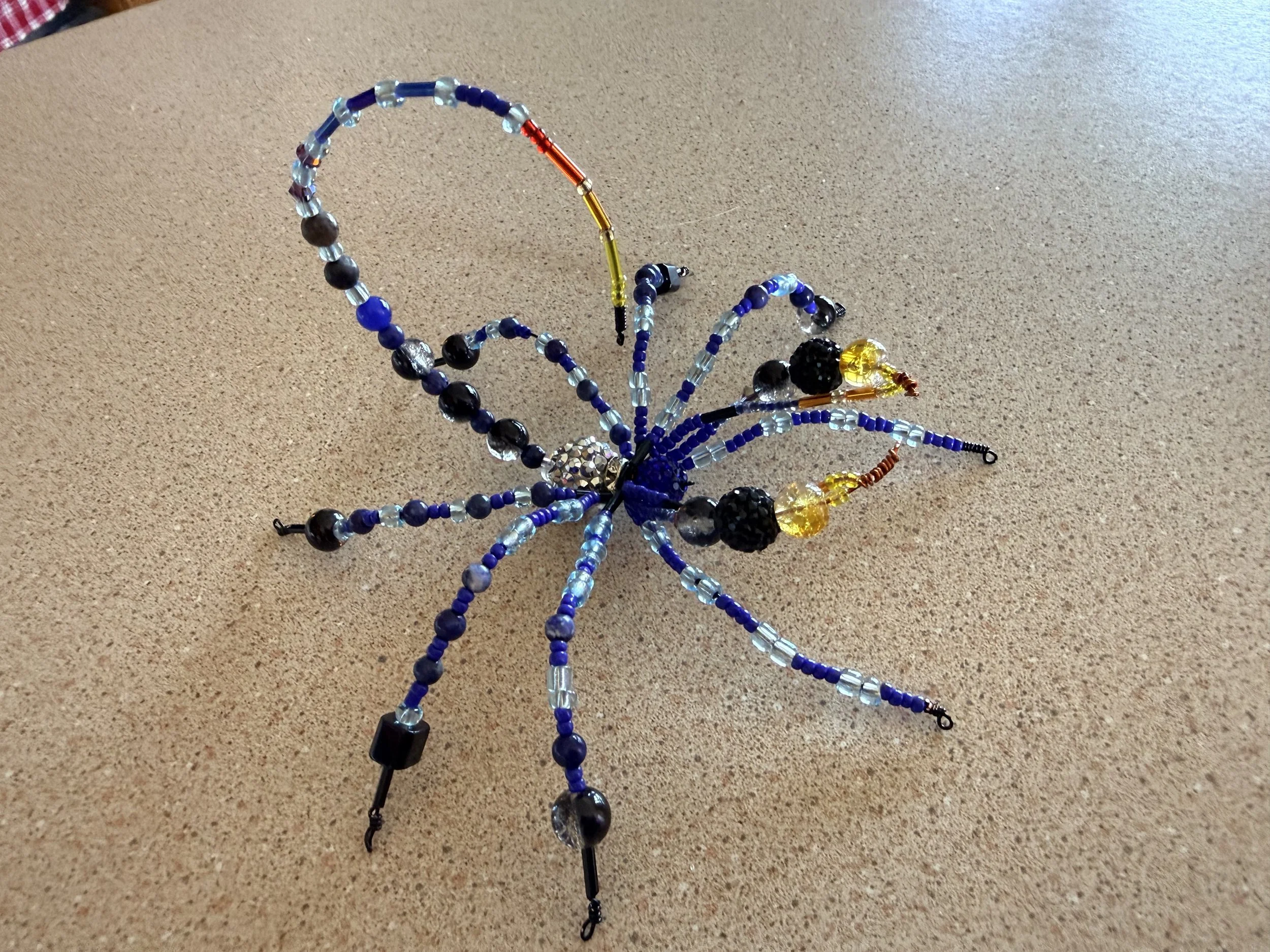 A decorative scorpion made of various colorful beads and wire, resting on a beige surface.