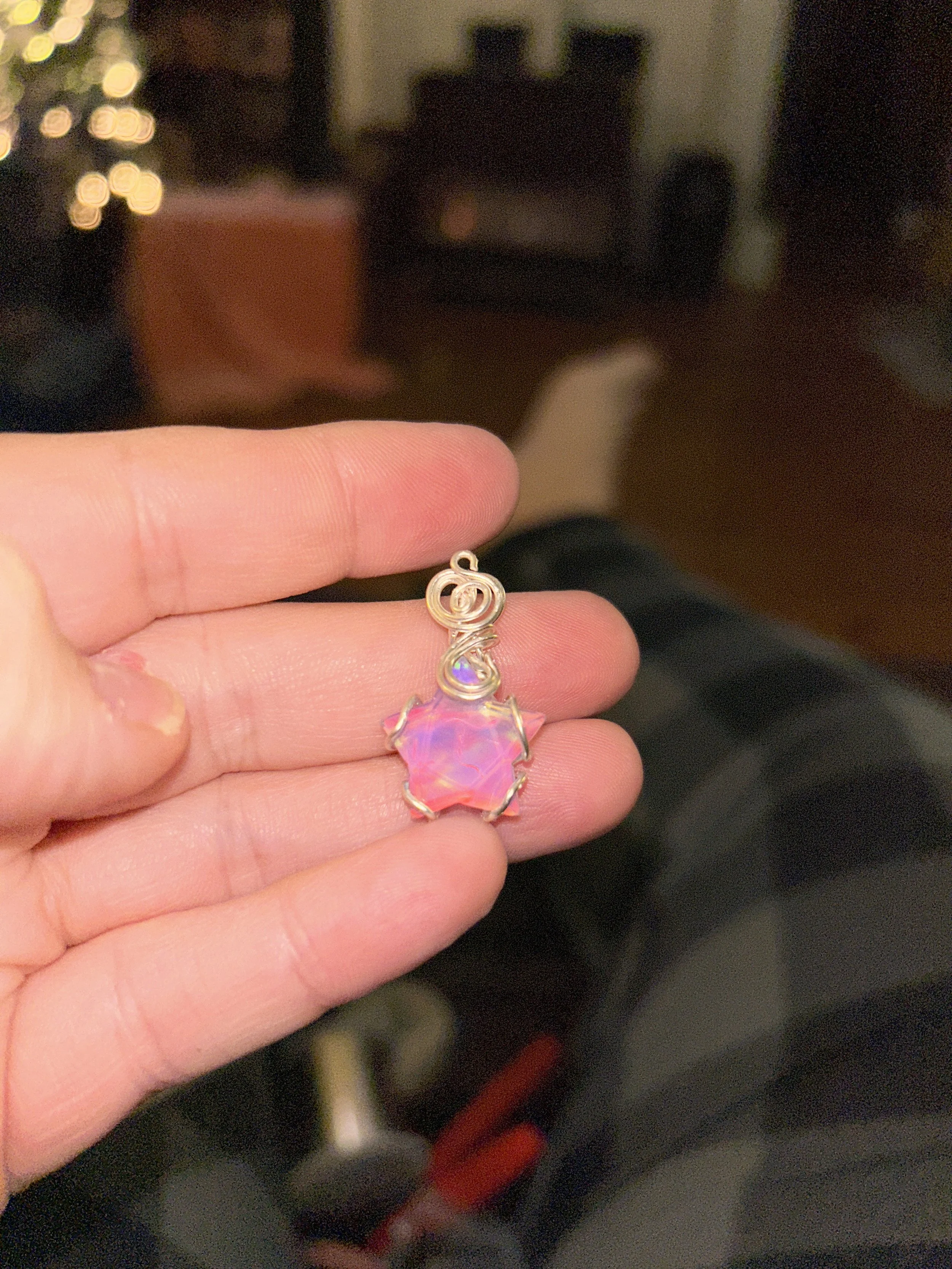 A hand holding a small silver charm with a pink and purple iridescent star-shaped gemstone.