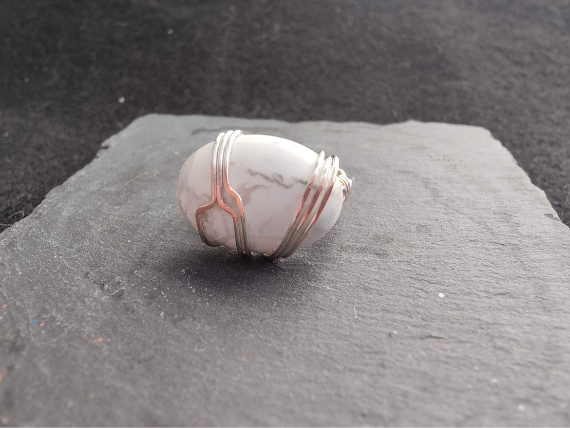 A white marble stone wrapped with silver wire, placed on a gray textured surface.