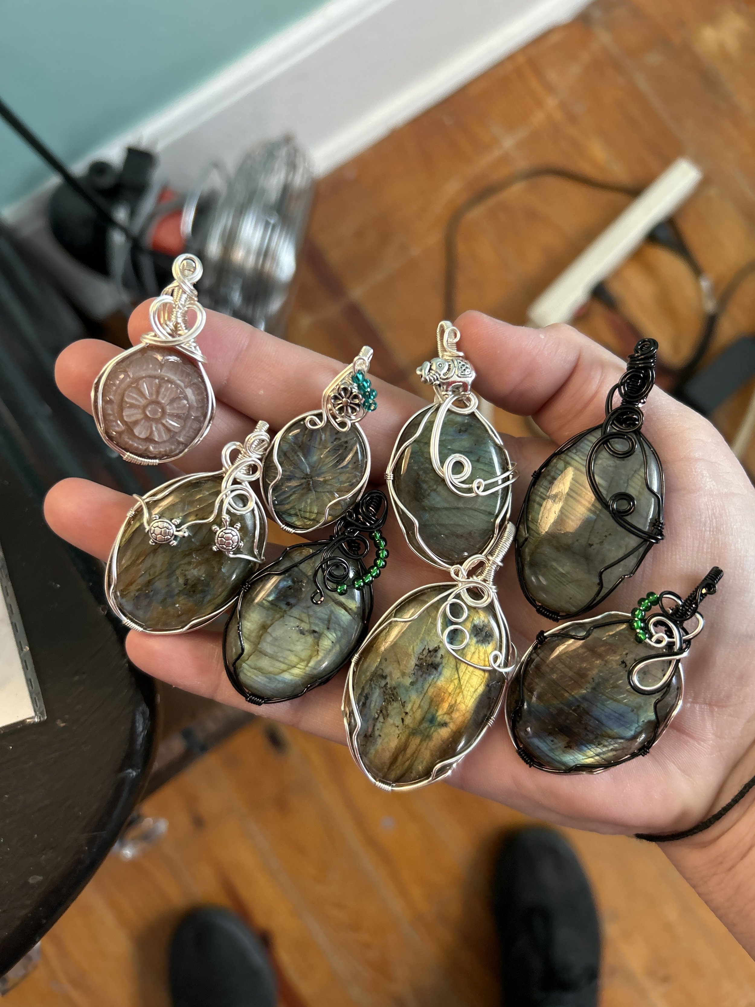 Hand holding several wire-wrapped gemstone pendants with labradorite stones and intricate wire designs.