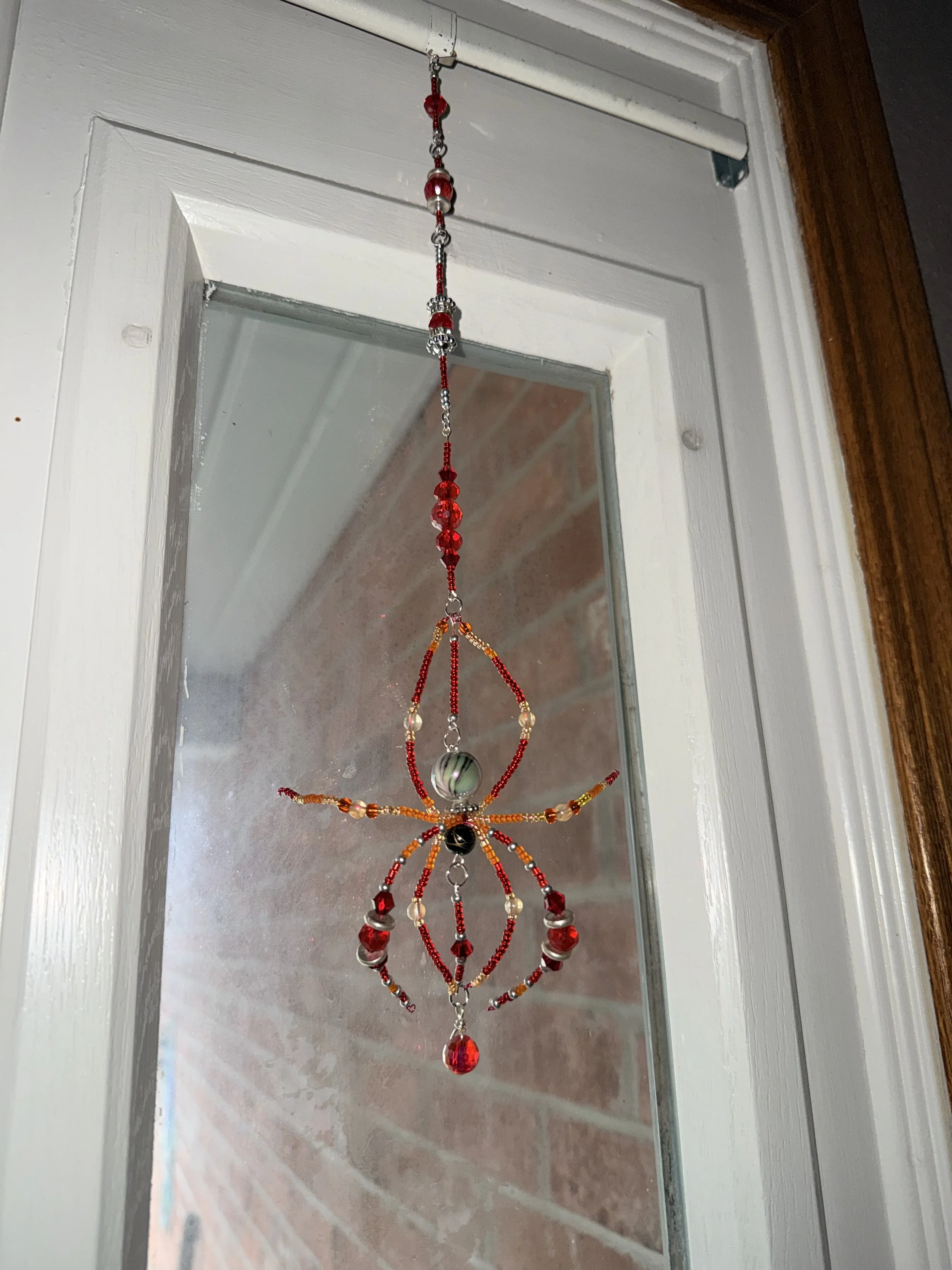 Colorful beaded ornament hanging inside a door frame, with a brick wall visible through the glass window.