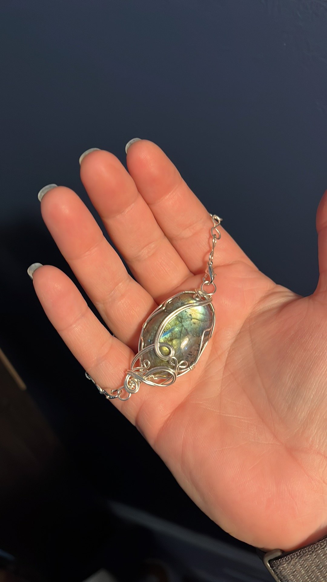 A hand holding a wire-wrapped pendant necklace with an iridescent stone.
