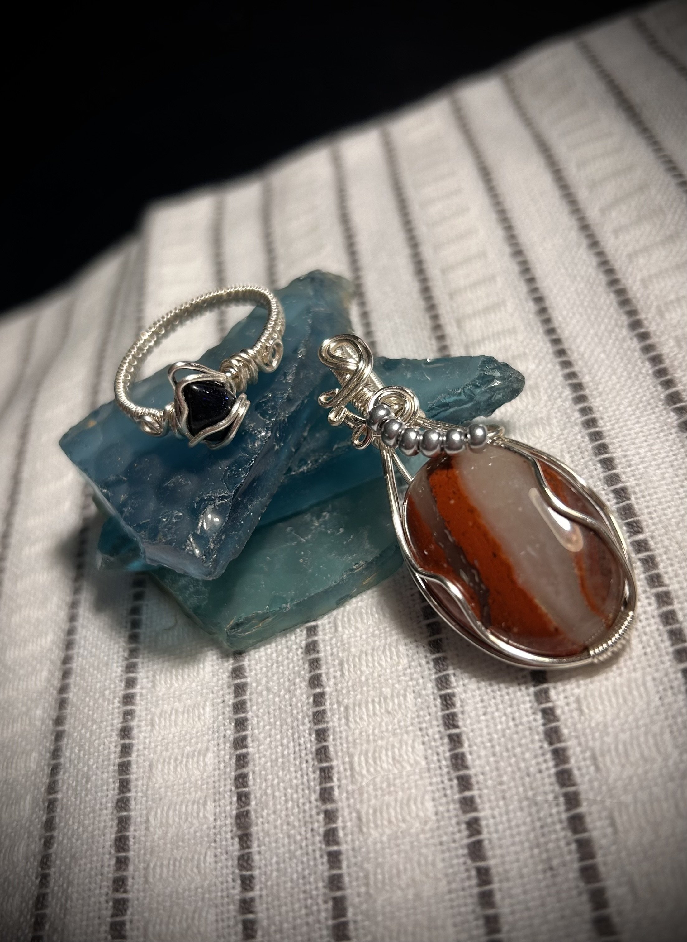 Silver jewelry with black and orange stones on a blue glass pieces, placed on a striped fabric surface.