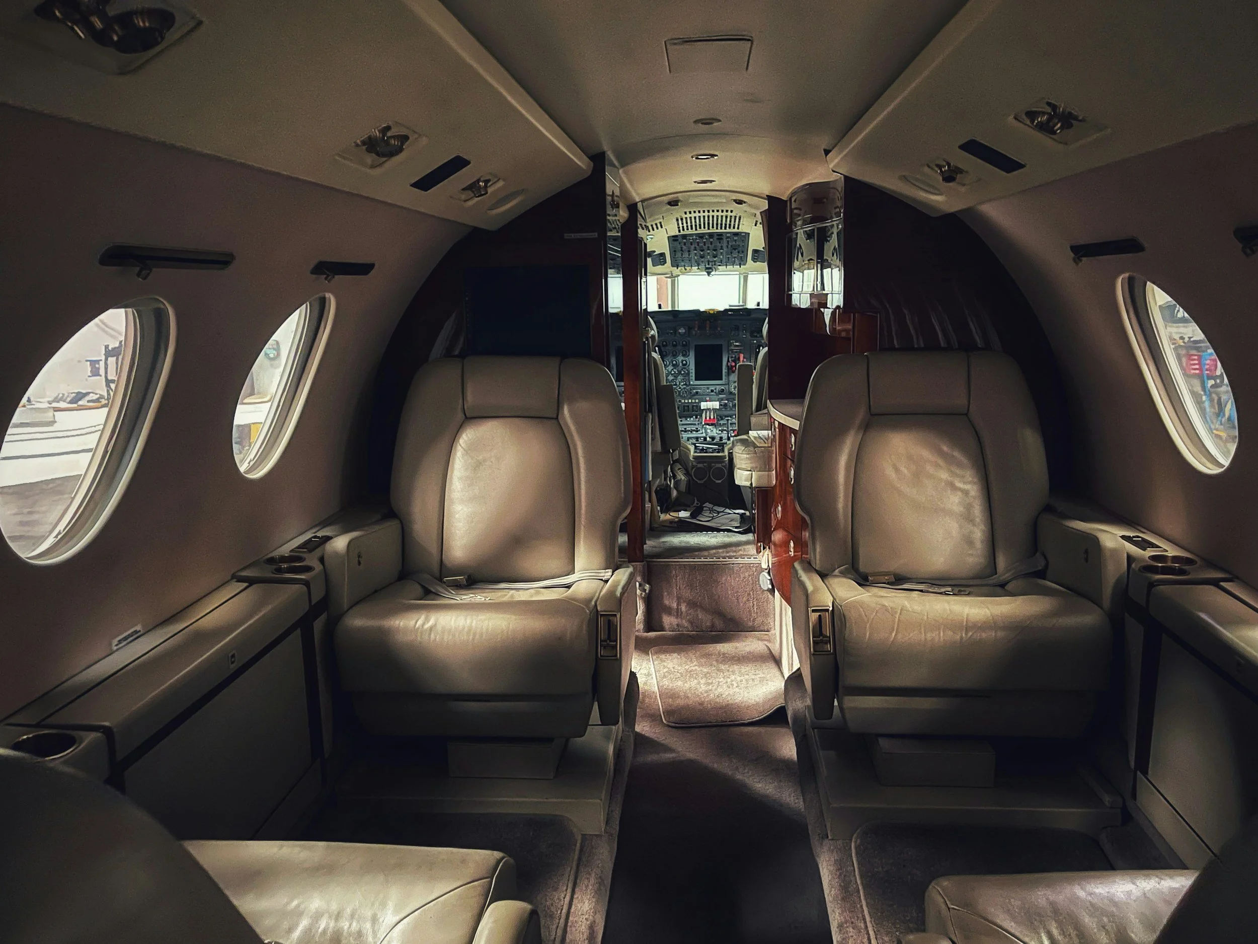 Interior of an airplane cabin showing beige leather seats, windows on the sides, and the cockpit in the background.