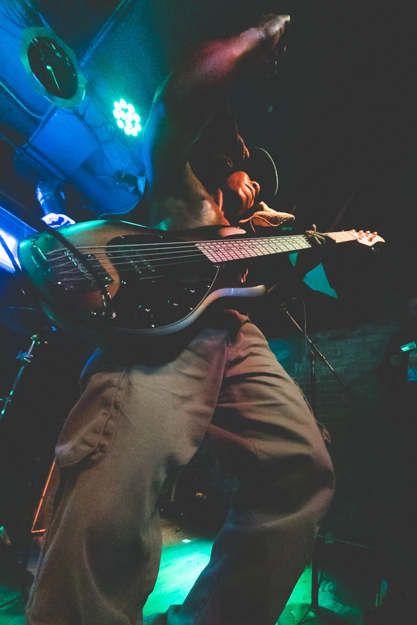 A person sitting on the ground playing an electric guitar, with colorful stage lights illuminating the scene in a dimly lit setting.