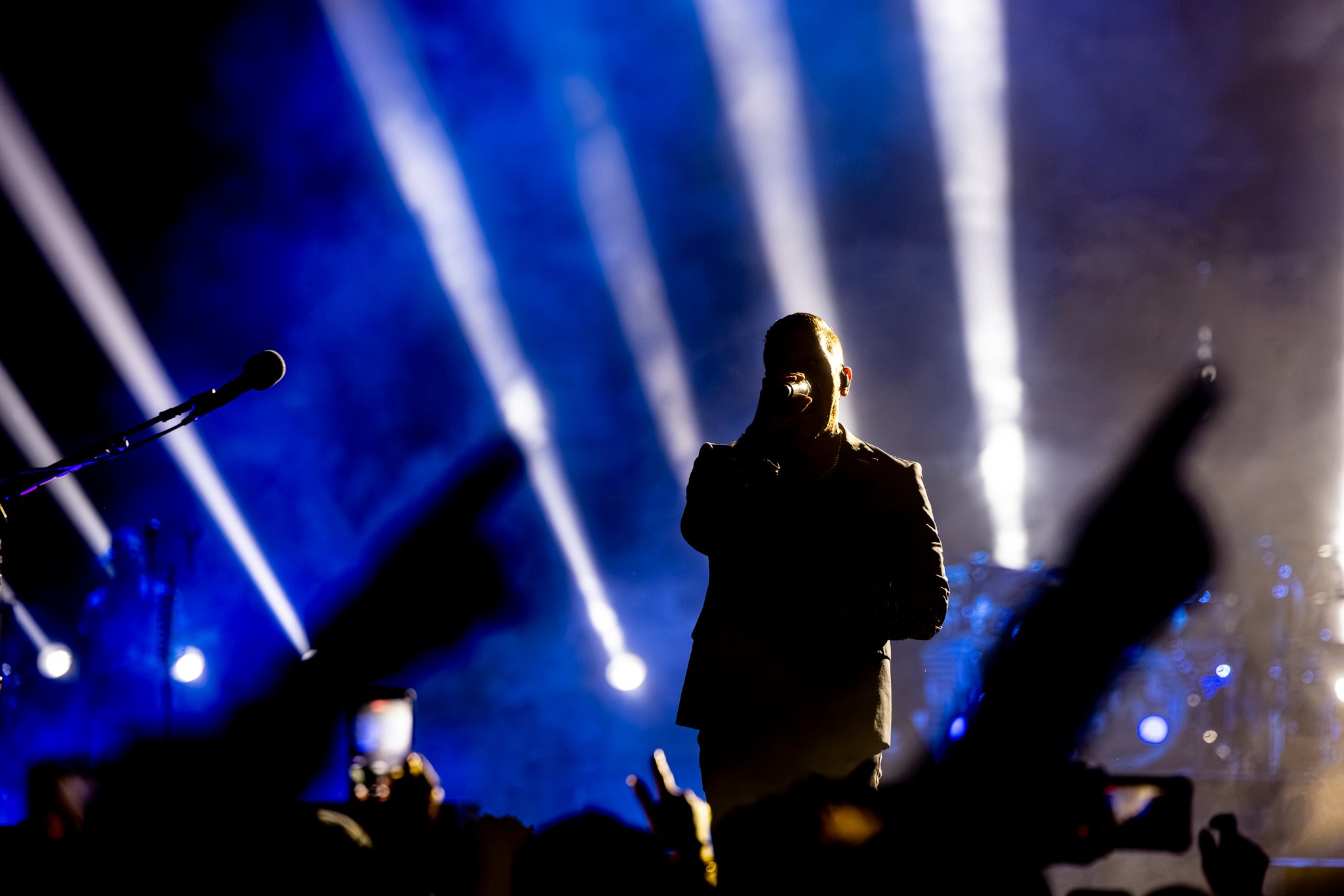 A singer performing on stage with bright blue and white lights behind him, and a microphone in front of him.