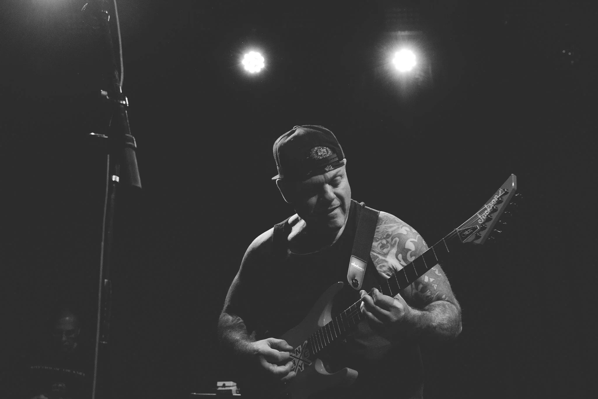 Black and white photo of a man wearing a hat playing an acoustic guitar on a dimly lit stage.