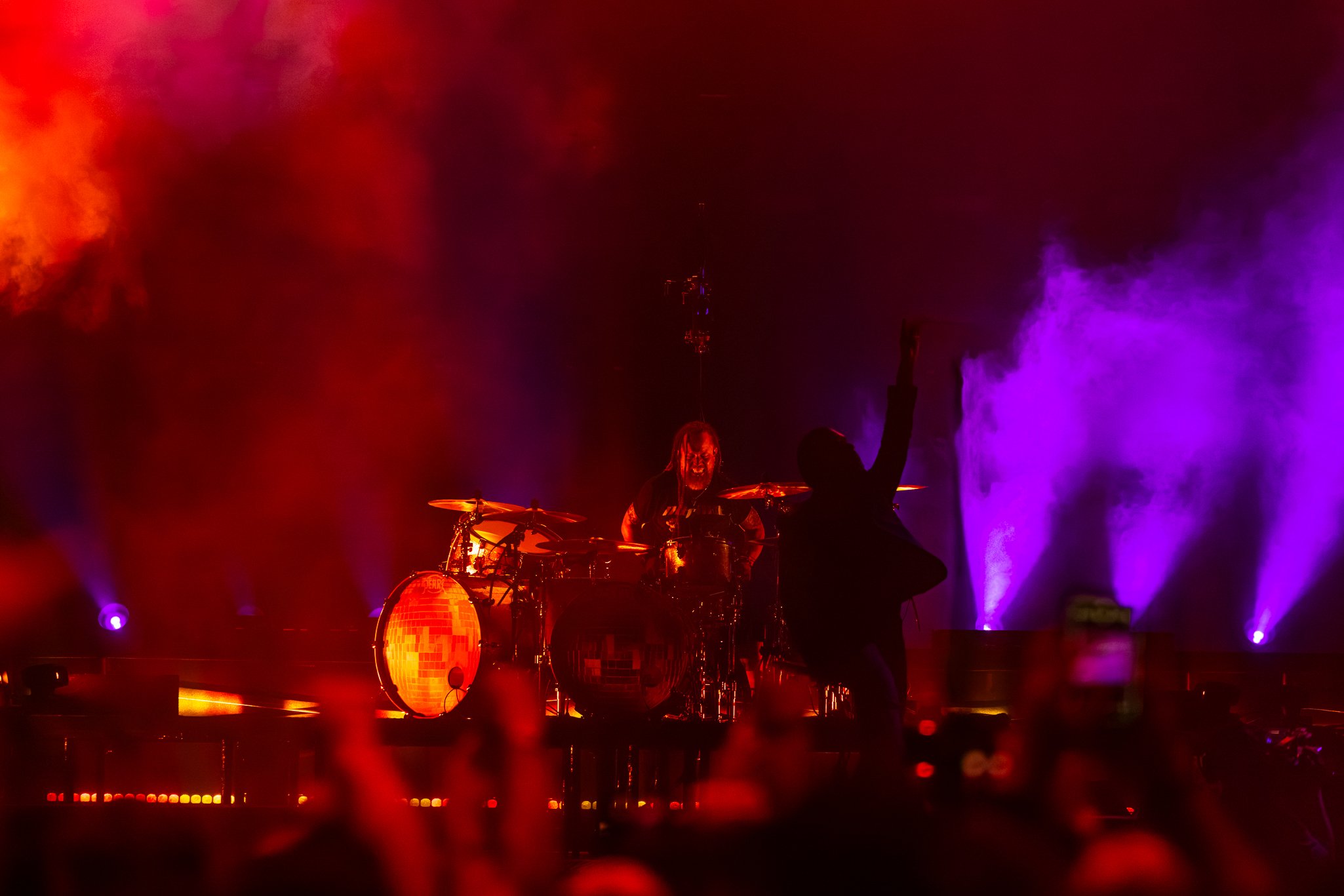 A musician playing drums on stage with colorful fog and lighting effects.