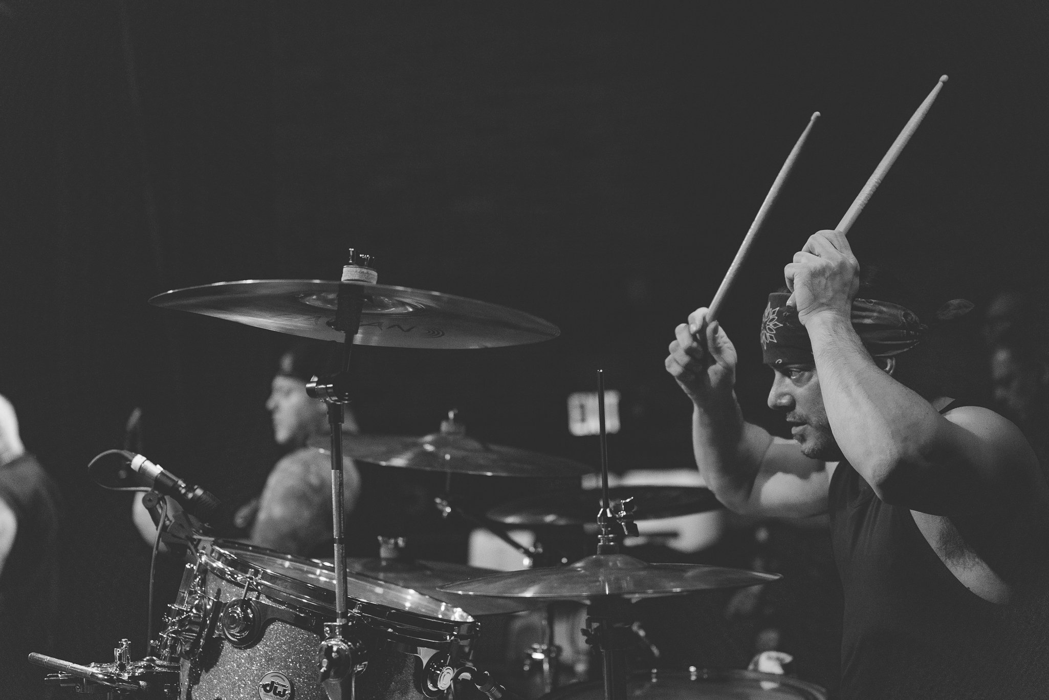 A musician in a band, wearing a bandana, playing the drums on stage during a performance.