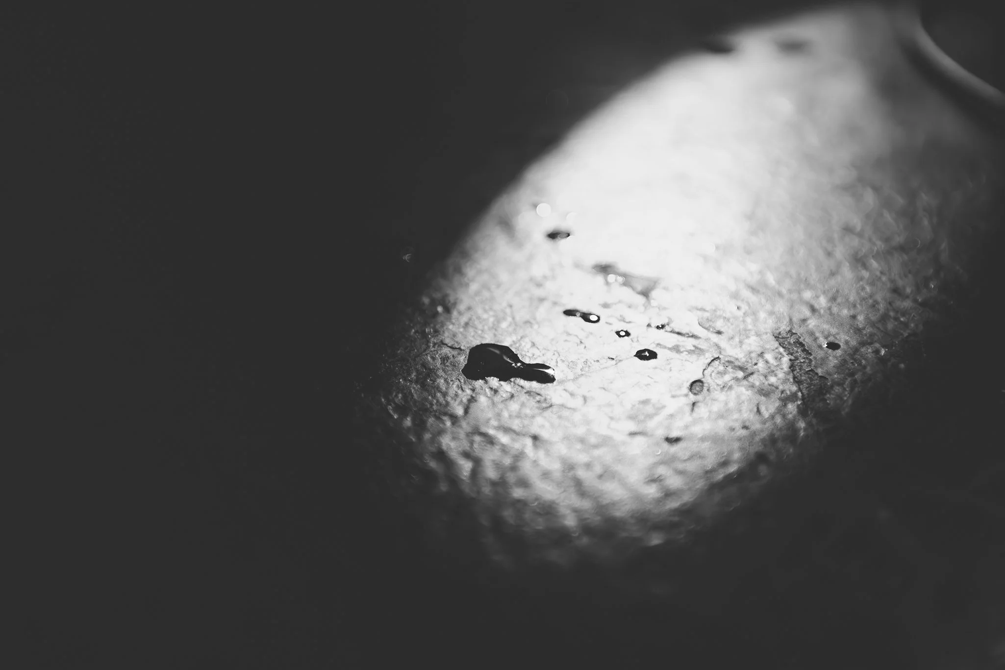 Close-up of a textured surface with water droplets on it, illuminated by bright light, creating high contrast and shadows.