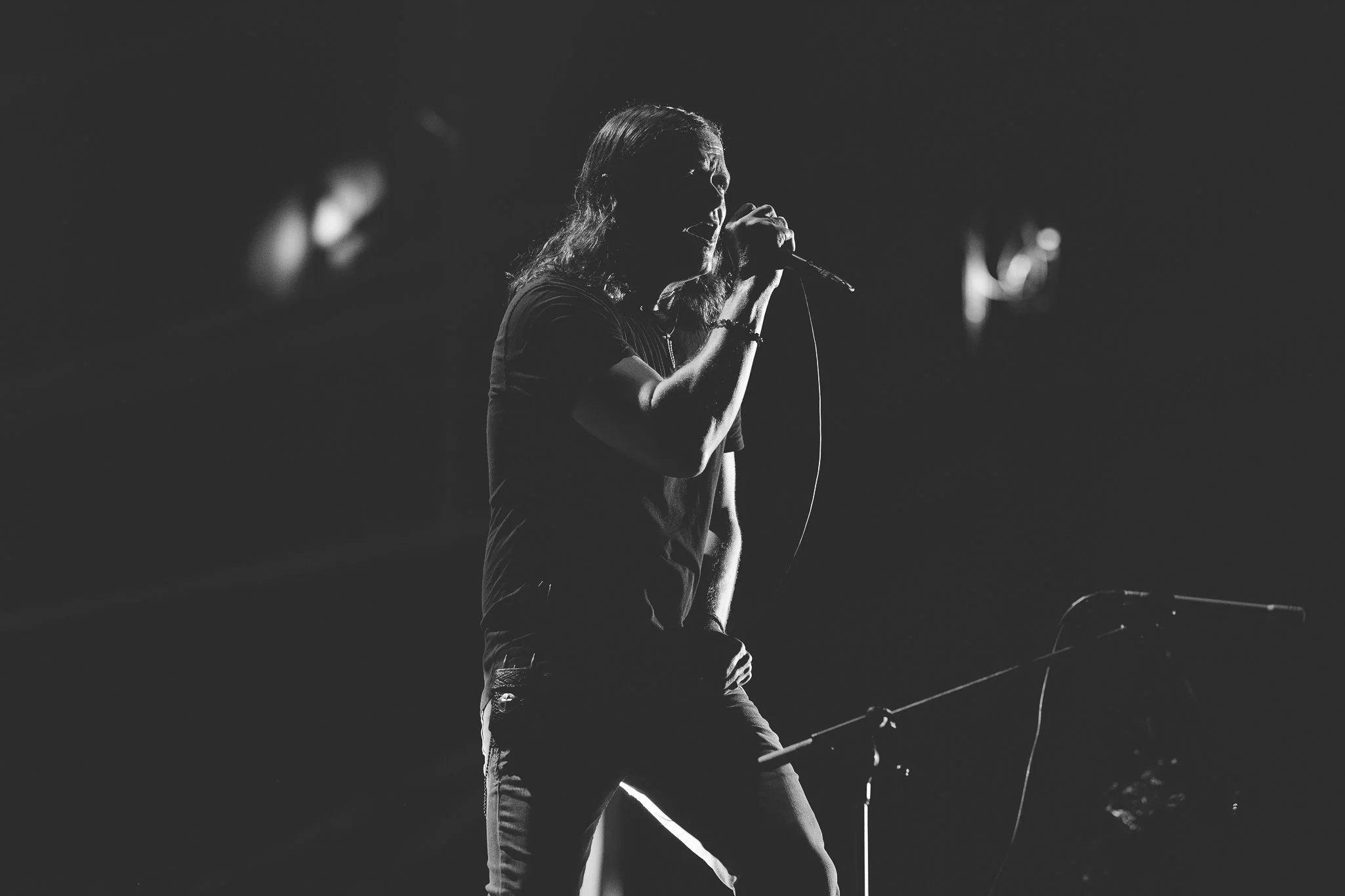 A woman singing into a microphone on stage, with a dark background and stage lights.