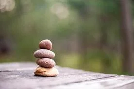 Stack of five smooth stones on a wooden surface outdoors, with a blurred green natural background.