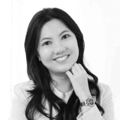 Black and white portrait of a woman smiling, with long dark hair, wearing a light-colored blazer, and a watch on her wrist.