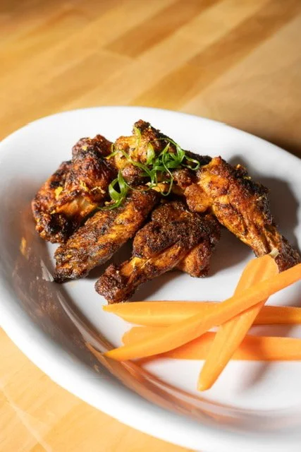 Fried chicken wings garnished with green onions served with sliced carrots in a white bowl.