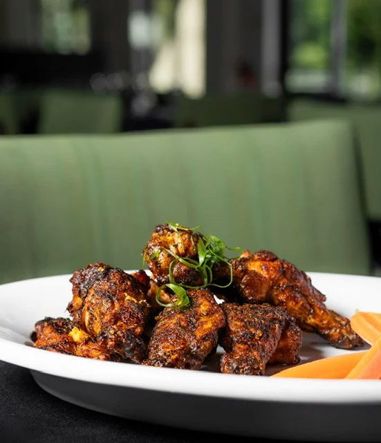 Plate of fried chicken wings garnished with green herbs and served with sliced carrots on the side.
