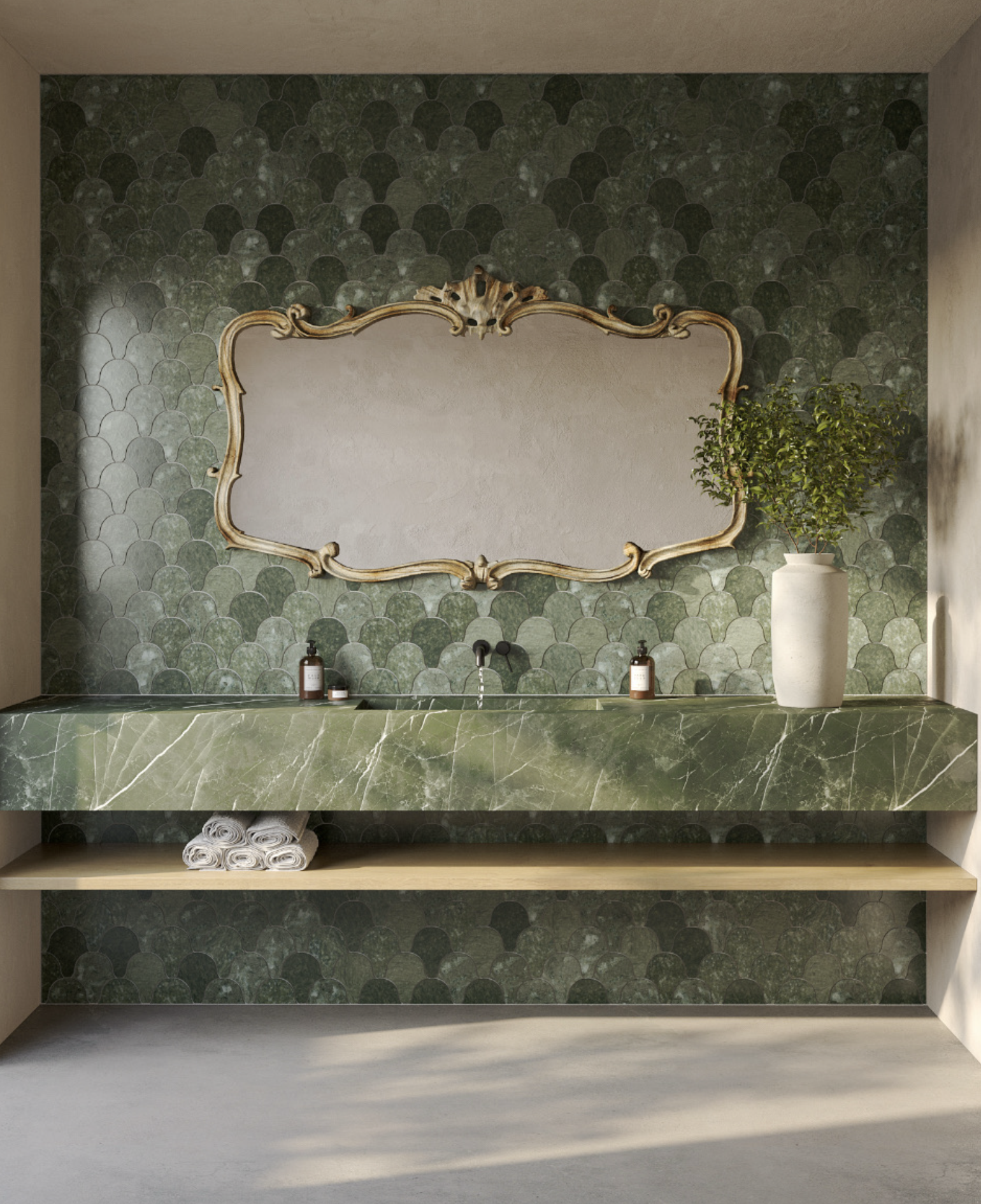 Green marble countertop with a gold-framed mirror on a green textured backsplash. A white vase with a green plant, brown soap dispensers, and rolled white towels are on shelves underneath.