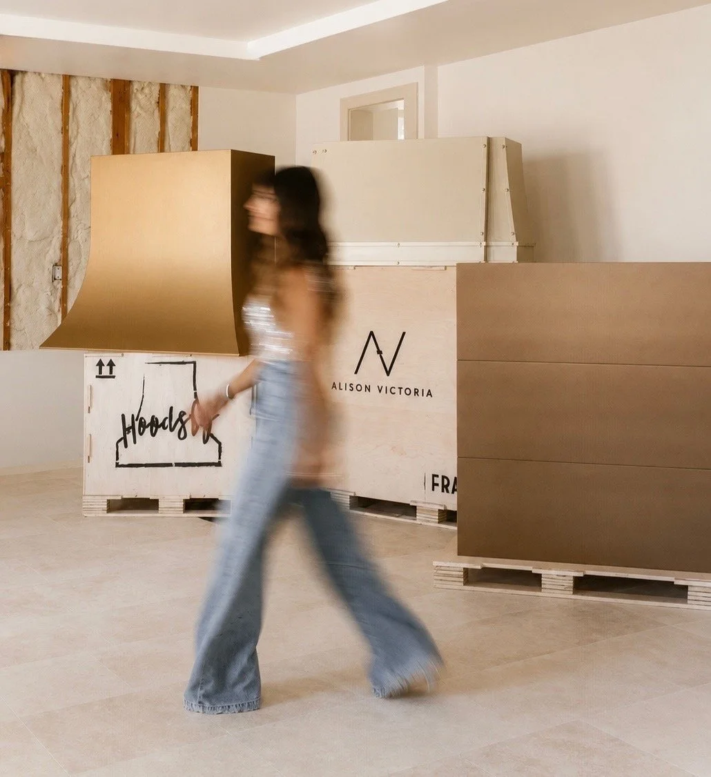 A woman walking past stacked wooden shipping crates in a room with a partially unfinished wall.