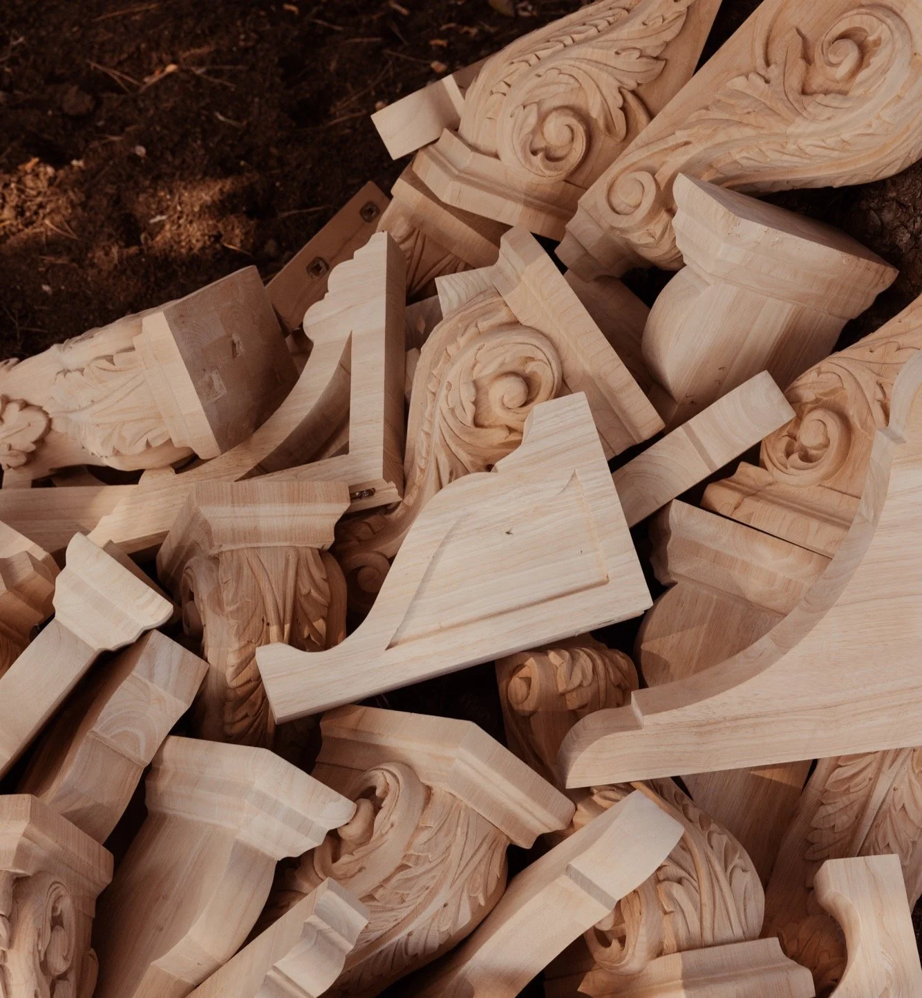Grouped unfinished wooden decorative corbels with carved swirling designs, stacked on a dark background.