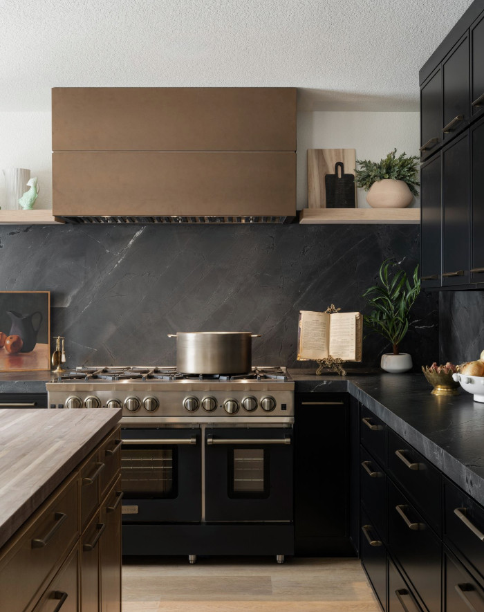 Modern kitchen with black cabinetry, a gray stove with a pot, and decorative items like plants, a framed picture, and an open book on the counter.