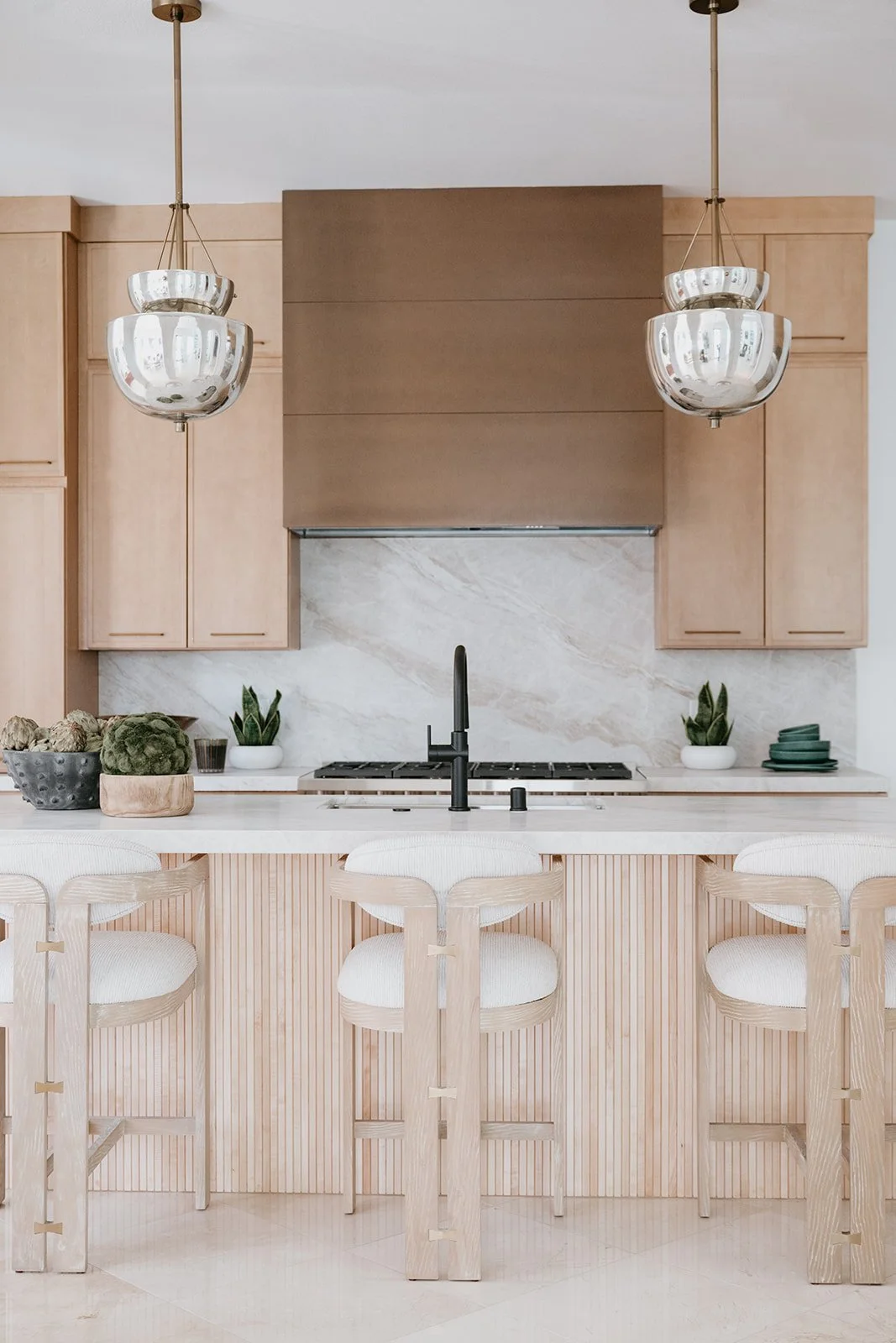 Modern kitchen with light wood cabinets, a white marble backsplash, two pendant lights, a black faucet, and white bar stools.