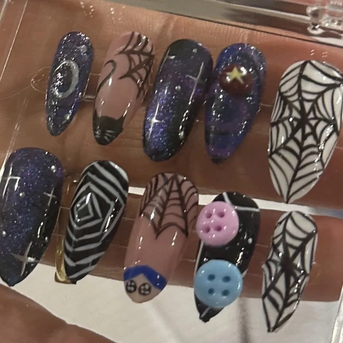 Nail art designs with Halloween themes, including spiders, webs, stars, and buttons, on a display stand.