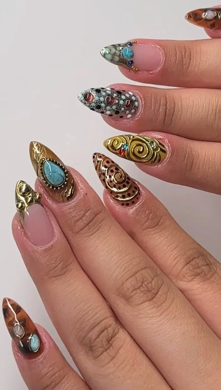 Close-up of a hand with elaborately decorated, long almond-shaped nails featuring various intricate designs and vibrant colors.
