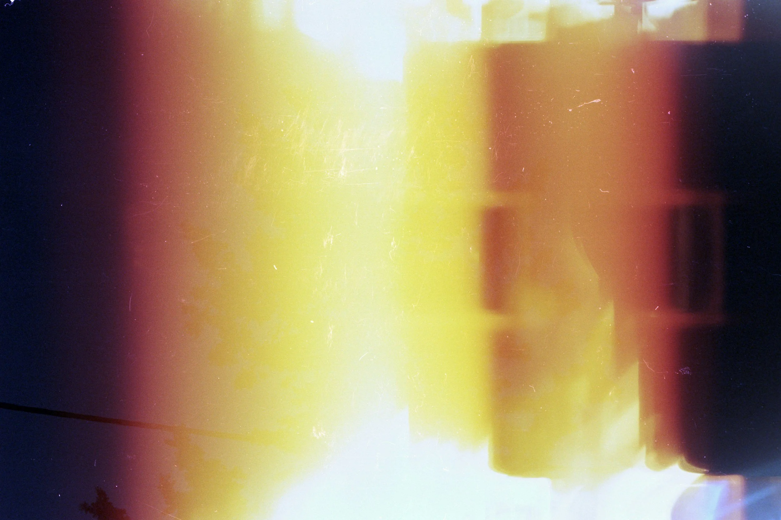 Blurred image with bright light at the center, transitions from yellow to orange and red, mixed with dark areas and light spots.
