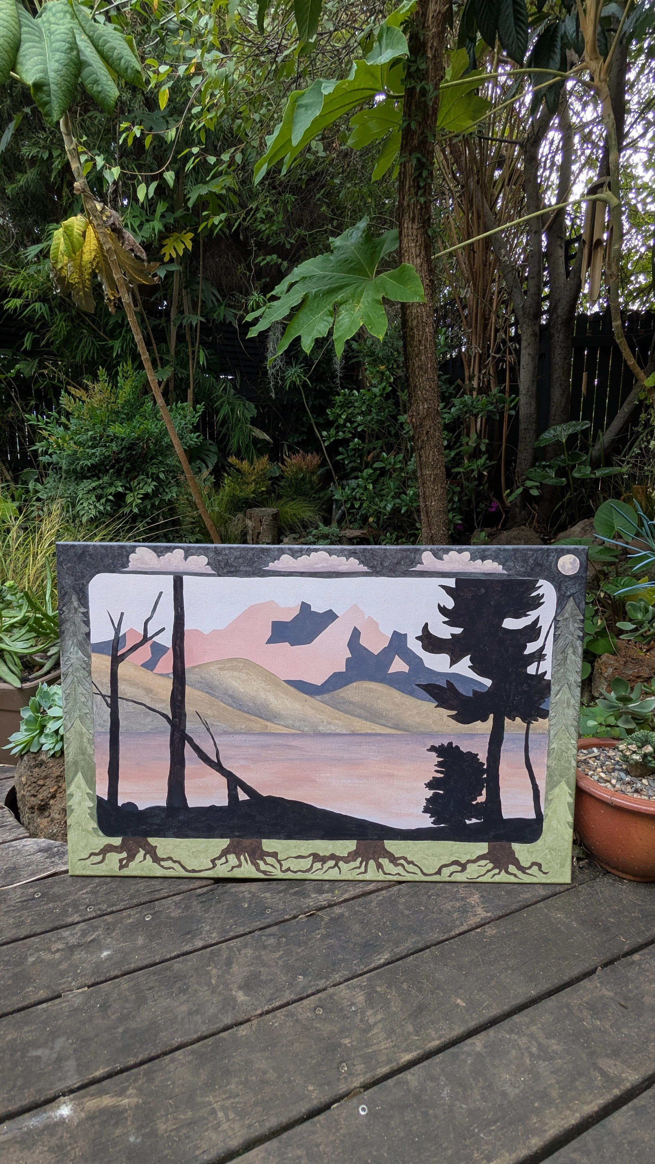 A painting of a mountain landscape with trees in the foreground, set against a pastel pink and purple sky, leaning on a wooden deck surrounded by plants and trees.