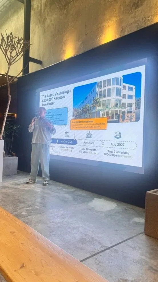 Person stands in front of a presentation screen displaying a timeline and images of a building project related to a kingdom investment.