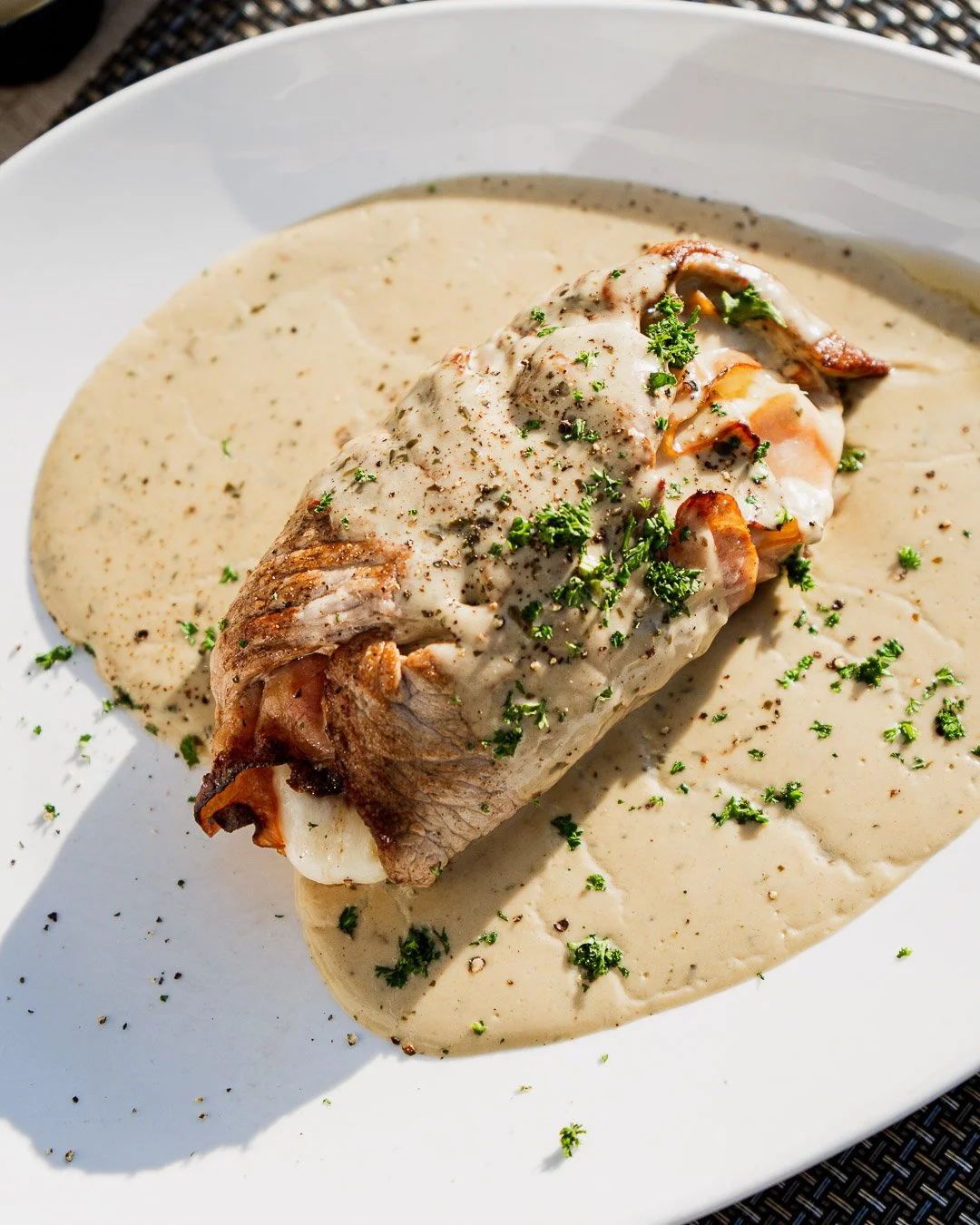 Baked fish fillet topped with creamy sauce, garnished with chopped parsley, served on a white plate