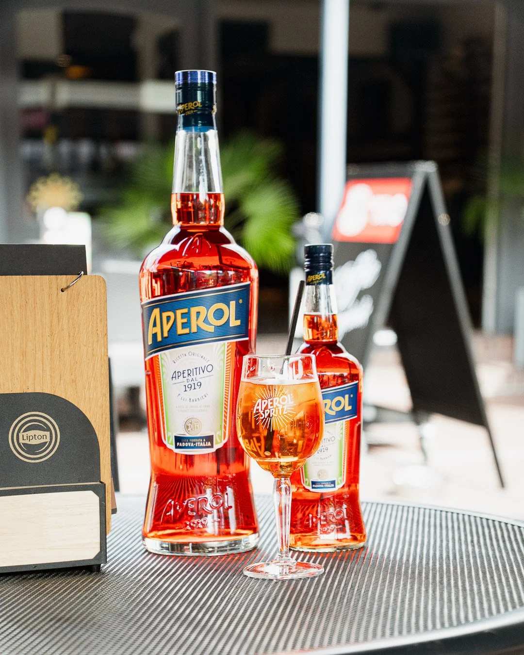Two bottles of Aperol and a glass of Aperol Spritz on a table at a cafe